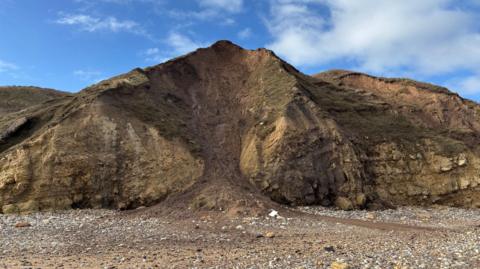 Stones tumbling down a cliff face on to a beach.