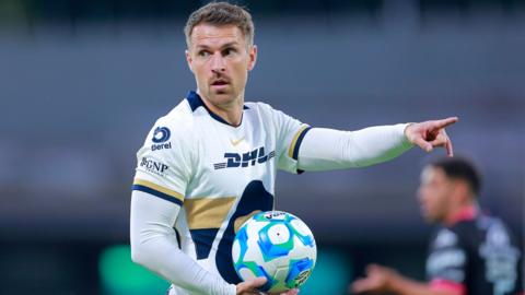 Aaron Ramsey holds the ball and points during his Pumas debut in Mexico