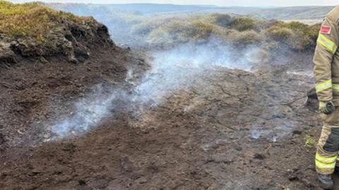 Smoke in the countryside with a firefighter to the right of the image.