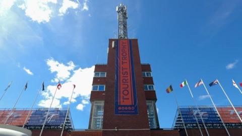 The red brick tower at the grandstand, which had flag at wither side and a banner that reads Tourist Trophy down the middle.