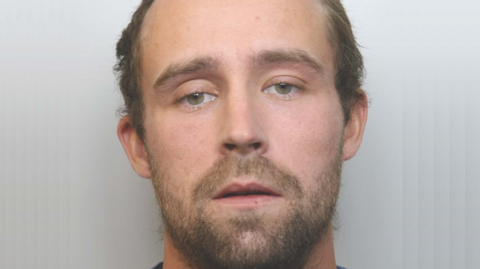A mugshot of Jordan Ellis. He has short brown hair and a short brown beard.