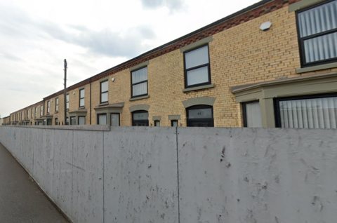 An image of the houses in Tunstall Street in 2022, while they were empty and hidden behind large grey hoardings. 