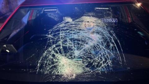 There is a windshield that has massive cracks in it, the car is red.