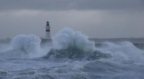 A lighthouse with crashing waves in stormy weather. 