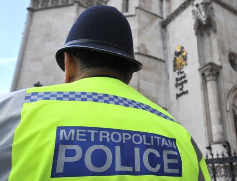 A police officer wearing a flourescent tabard with his back to the camera, standing outside a court building.