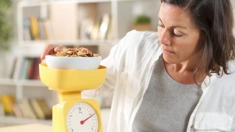 A woman weighing a bowl of food on a scale.