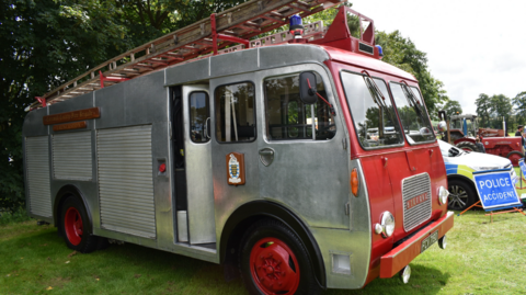 A picture of a vintage fire engine. It is silver and red in colour and has the force logo on the side of the vehicle. 