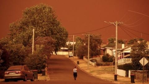 A woman walks down a street in Bruthen, Victoria, beneath an orange sky