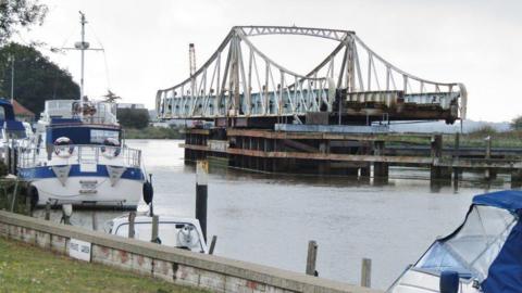 Reedham swing bridge open for river traffic. Blue and white boats are moored on the river bank