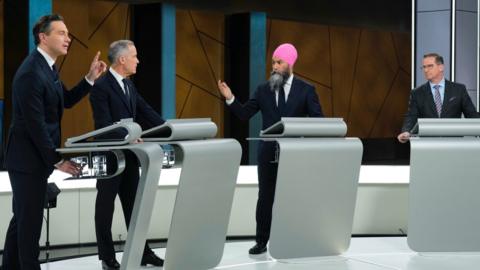 Pierre Poilievre, Mark Carney, Jagmeet Singh and Yves-François Blanchet stand behind podiums wearing suits as they debate.