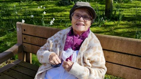 A woman sitting on a bench, smiling to camera