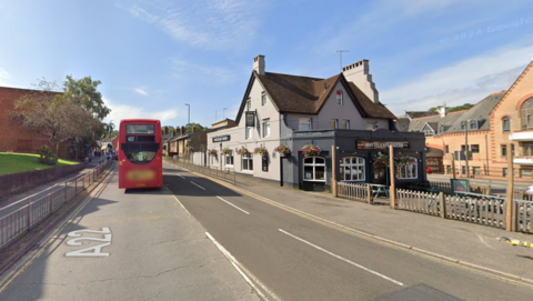 A Google Street image of a road running alongside a grey pub with a beer garden out the front.