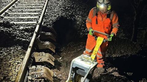 A man in high visibility clothing and a machine working on a rail line in the dark.