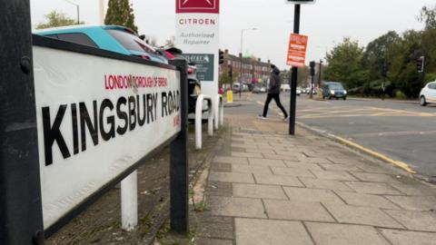 Kingsbury Road road sign and a pedestrian crossing the road