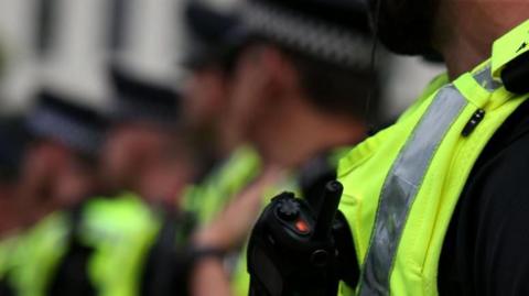 A blurred image of police officers wearing yellow vests standing in a line