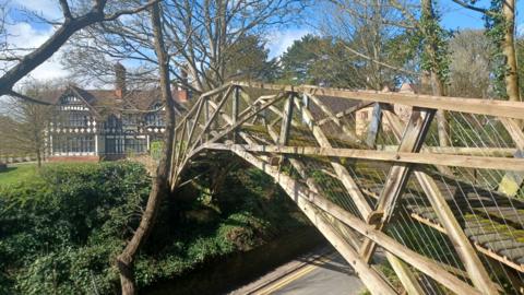 Close-up of the restored wooden bridge with a house in the background and trees and foliage next to it. 