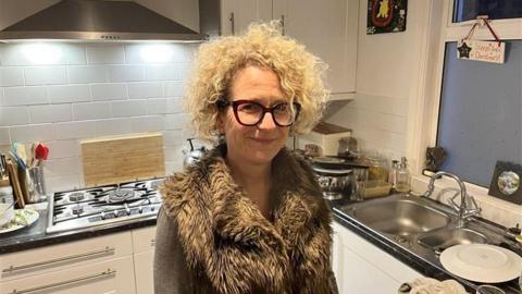 A blonde woman standing in her kitchen.