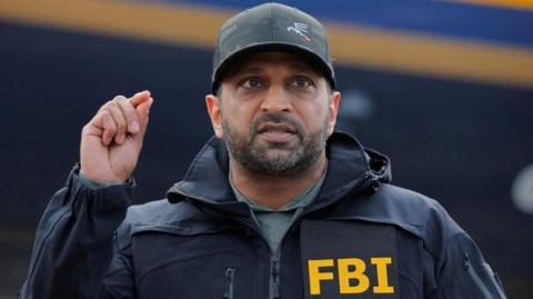 Kash Patelgestures while wearing a baseball cap and an FBI branded jackte