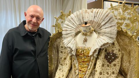 Stephen Rodwell stood next to an Elizabethan era dress which is cream coloured.