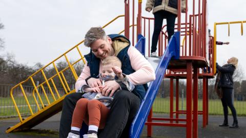 A man and a young child on a slide in a playground.