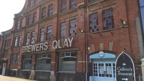 The old Brewers Quay building. It is a large red brick brewery with a sign reading Brewers Quay.