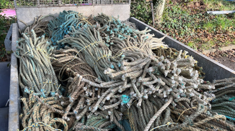 The back of a truck filled with long rows of tied up rope parked in a car park.