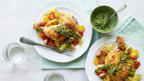 A plate of roast chicken legs with potatoes, fennel and tomatoes, with a small bowl of salsa verde on the side.