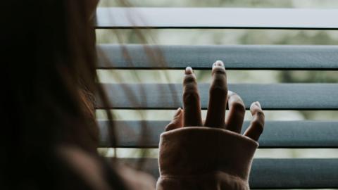Woman looking out the window blinds