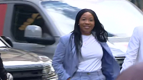 A woman pictured smiling and walking. She is wearing a light purple suit and white t-shirt. She has chest length straight black hair.