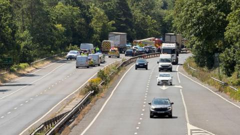 Emergency services including police and firefighters at the scene of a crash on the A38 in Devon. Several other cars, vans and lorries are on the road.