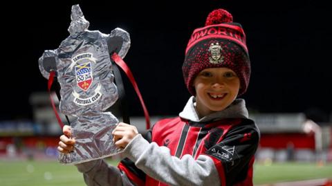 A young Tamworth fan holds up a tinfoil FA Cup trophy