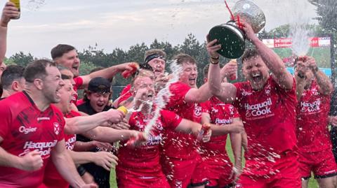Jersey players spray champagne while lifting the Siam Cup