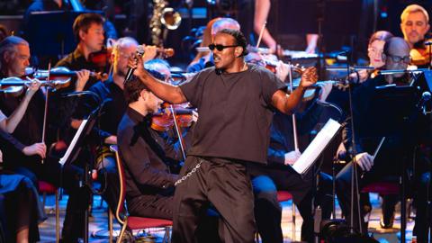 Luke James, dressed all in black, singing in front of a concert orchestra