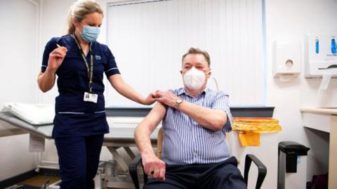 Advanced nurse practitioner Justine Williams (L) talks with 82-year-old James Shaw, after he became the the first person in Scotland to receive a dose of the AstraZeneca/Oxford Covid-19 vaccine, at the Lochee Health Centre in Dundee on January 4, 2021. 