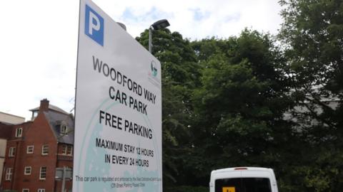 A close-up shot of a sign that reads: 'Woodford Way car park. Free parking. Maximum stay 12 hours in every 24 hours.'