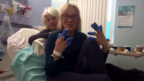 Louise Minchin holds up her bandaged hands while lying in a hospital bed.