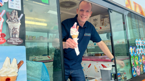 A smiling man stood inside an ice cream van holding a Mr Whippy 
