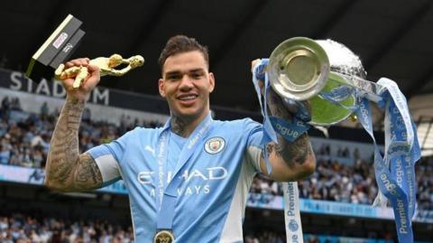 Ederson smiles while holding the Golden Glove and Premier League trophy in 2022