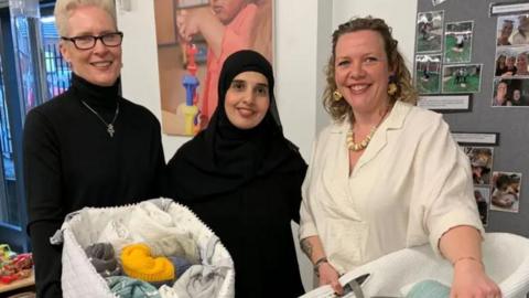 Prof Sally Pearse of Sheffield Hallam University (left, wearig a black jumper and holding a basket of coloured blankets), Lina Mohsen, a mum who has benefited from the scheme (middle, wearing a black hijab), and Cat Ross, Baby Basics chief executive (right, wearing a white top and holding a moses basket).