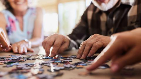 Close up of unrecognisable group of people playing with jigsaw puzzles at a care home.