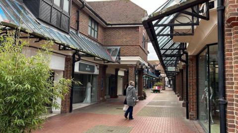 A open air mall with red brick shops. A woman is walking down a lane and looking in a shop window. 