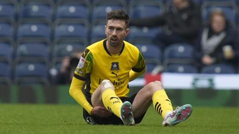 Plymouth Argyle striker Ryan Hardie sits on the pitch and holds his back