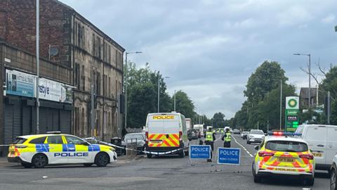 A police scene in Paisley - there are vans, police cars and ROAD CLOSED signs across the area, and officers in high vis vests standing at the scene