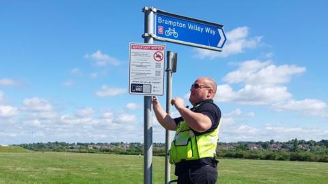 Police officer installing signage to warn against motorcycle nuisance