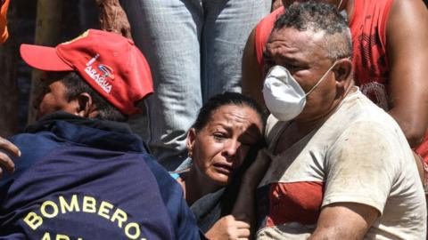 The sister of a man whose body was recovered cries as she is consoled by other people on October 11, 2022 in Las Tejerias, Venezuela. Search for missing continues two days after deadly landslides caused by heavy rains hit the town of Las Tejerias, 68k from Caracas