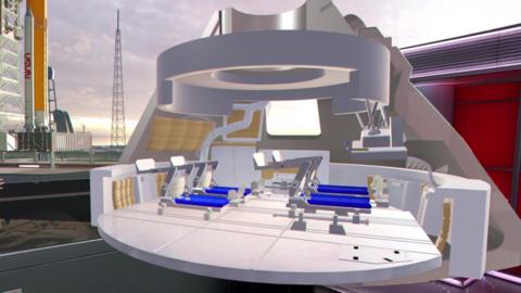 Rebecca Morrell stands to the bottom left corner of the image in a red and black spotty dress. She is gesturing towards a CGI image of the inside of the orion cpasule