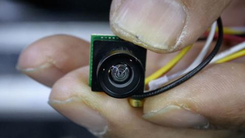 A spycam being held in someone's hand, showing it is not much bigger than a fingernail