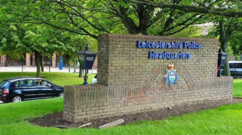 Wall outside Leicestershire Police's headquarters bearing the force's crest, surrounded by grass