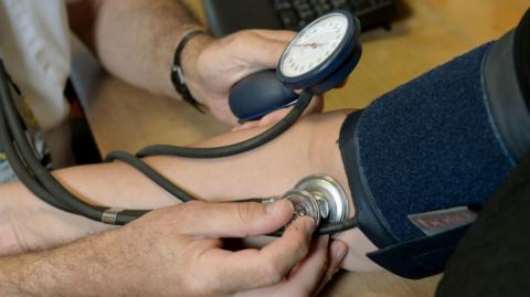 Close-up of a healthcare worker measuring a person's blood pressure using a cuff, gauge and stethoscope during a health check.
