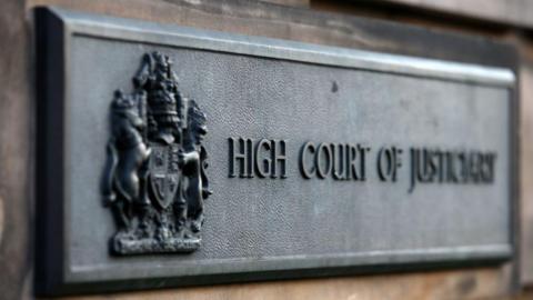 The heavy brass plaque at the High Court building in Edinburgh. The coat of arms of the court is in the foreground with the title moving into the background